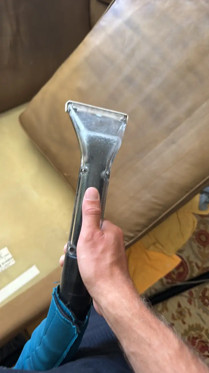 Hot water extraction tool lifting soil from the beige microfiber sofa