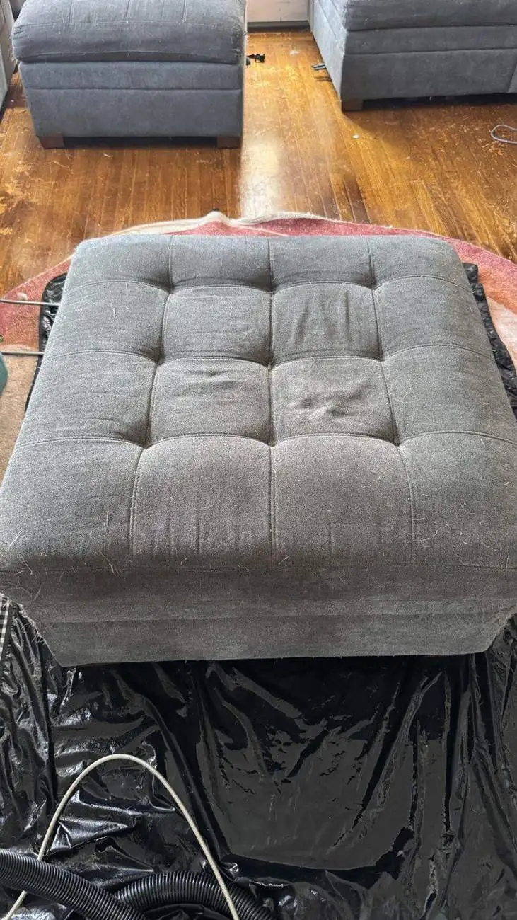 Gray tufted ottoman before cleaning, matted and dirty
